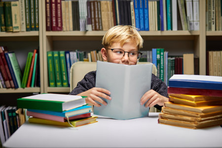 clever kid boy while reading book in library after school classes, doing homework