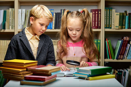 two friendly school kids discussing a book while reading in library, education concept. child brain, knowledgeの写真素材