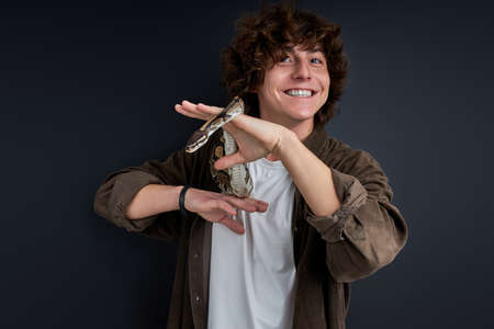 python snake coiling around mans hand, cheerful guy enjoys, likes exotic animalsの写真素材