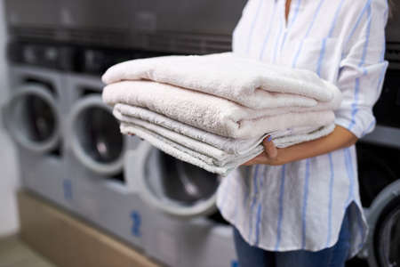 cropped woman is holding a stack of white towels. female in washing house. concept of service in hotels, laundry, spaの写真素材
