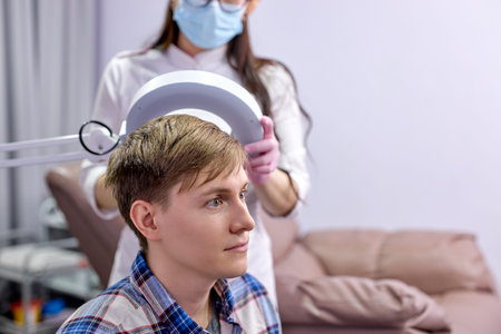 female trichologist using dermatoscope while examining male head and hair. in bright cosmetology...