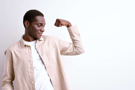 afro american guy showing arm muscles, powerful strong man isolated on whiteの写真素材
