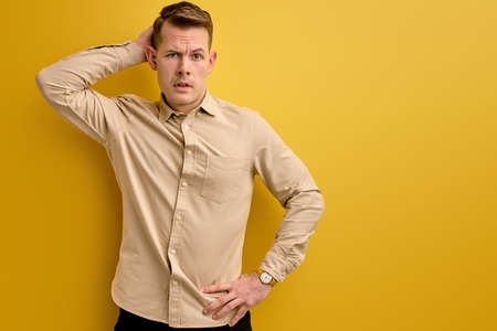 doubtful young caucasian guy stand thinking, scratch back of headの写真素材