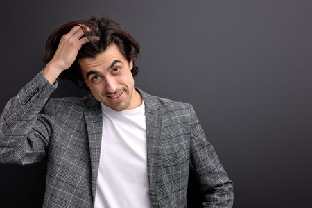 glad millennial guy in beautiful wear suit looking at camera touching hair