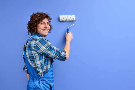 Paint rolling. Decorator hold paint roller in hands. Man in working clothes repairing wallの写真素材