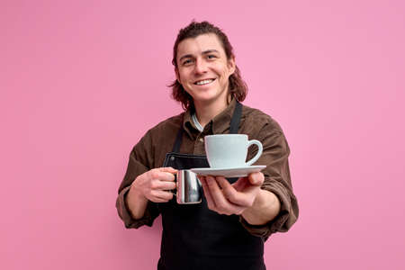 Here your latte. Portrait of positive cheerful caucasian guy student work part-time in coffee bar shopの写真素材