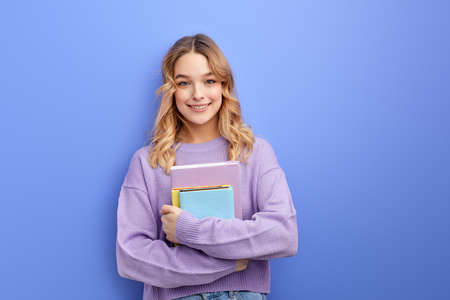 Cheerful beautiful teen student girl hold books isolated on pastel blue background studio portraitの写真素材