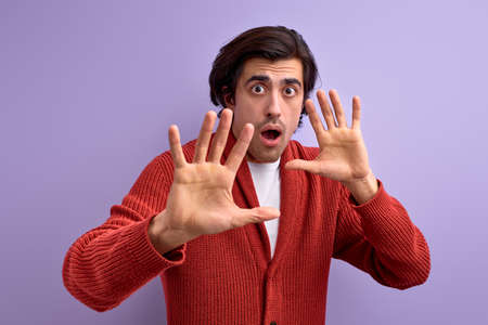 Afraid young man in defense attitude gesturing stop with hands, isolated on purple backgroundの写真素材