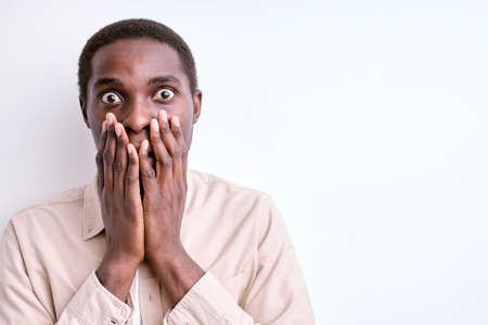 shocked african man stand in fear, frightened by something, closing mouthの写真素材