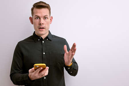 surprised guy in casual green shirt hold smartphone in handsの写真素材