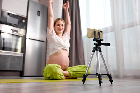 calm caucasian pregnant female sit doing exercises on floor and recording video