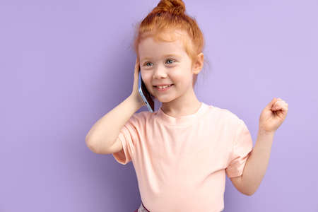 little redhead girl talking on phone indoors. concept of addiction of children and gadgetsの写真素材