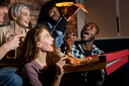 friendship, people, entertainment and junk food concept - happy friends eating pizza and watching movie or tv series at homeの写真素材