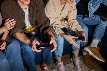 Diverse Students enjoying of playing in video game having rest at home. Smiling surprised excited american people have fun with joysticks in living room interior, free space, close-upの写真素材
