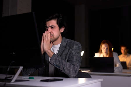 Portrait of exhausted serious caucasian male worried by work on computer in office at night, miss the deadline, has a lot of troubles, in dark room, sit thinking. work, business conceptの写真素材