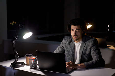 Thoughtful Man Read Business Plan on Computer, Thinking About Question Or Task By Boss, Man Realising Amount Of Work In Office At Late Night, Side View. In Dark Office Roomの写真素材