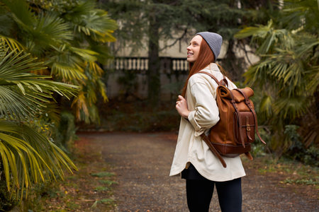Seen from behind modern tourist woman with backpack having excursion in garden or forest full of...