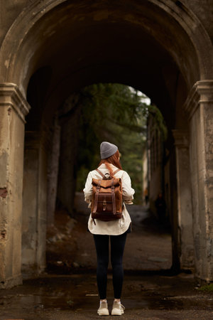 rear view on traveler woman with backpack stand in historical ancient arch, exploring interesting...