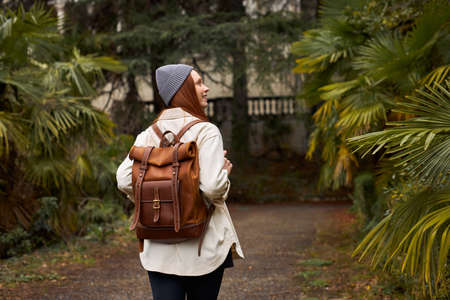 Caucasian European redhead woman tourist with backpack travels, enjoying beautiful nature while walking alone in forest, garden, historical sites. Rear viewの写真素材