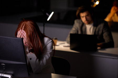 Sleepy exhausted young caucasian man working late night at office desk with pc, eyes are gonna closing and female is about to fall asleep, sleep deprivation and overtime overload working concept.の写真素材