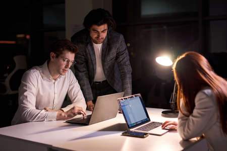 Responsive directore or manager of company help co-workers to meet the deadline, having no time to sleep and have rest, side view on business people working on startup project together, using laptopの写真素材