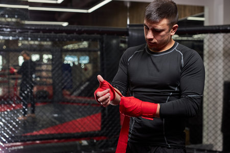 Confident Caucasian Male Kickboxer Fighter Preparing For Fight, Wrapping Hand In Red Bandage, Get...