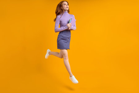 Dreamy redhead lady at weekend jumping, hold notebooks in hands on way home, in air, wearing casual...