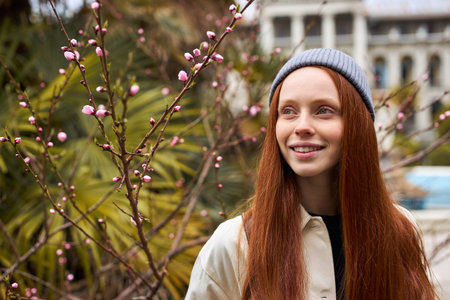 Close-up portrait of woman in spring garden. Springtime. Trendy redhead female enjoy feeling smell...