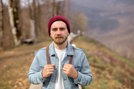 Traveler man with backpack walking alone in nature. Freedom concept. Copy space. Young caucasian bearded male in denim jacket enjoy landscapes. Travel, adventure, nature conceptの写真素材