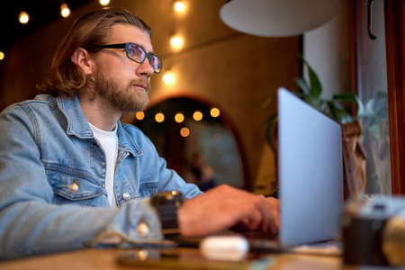 Side View Portrait Of Handsome Caucasian Guy In Denim Jacket Working On Laptop, Focused On Work, Side View portrait. Hipster Man Enjoy Working On Freelance, Thinkingの写真素材