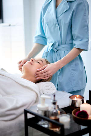Woman enjoying facial massage. Pretty female getting professional skin care at wellness center. Relaxation, beauty, spa and face treatment concept, copy space. side viewの写真素材
