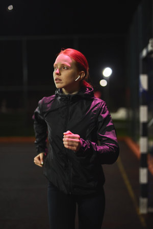 Beautiful Slim Fitness Woman in Black Athletic Wear is Jogging In Night City Street. Female is Doing...