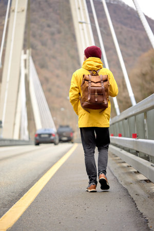 Man in yellow coat walking alone on pedestrian pathway on bridge in an urban park. Healthy...