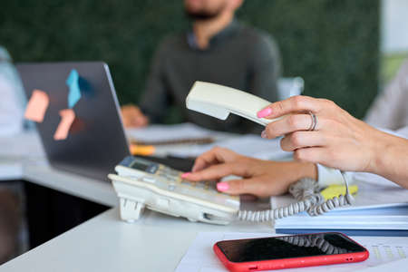 Closeup of cropped businesswoman pressing number button at office desk, dialing voip phone. people colleagues working in bright moder office desk, going to have conversation, discuss businessの写真素材