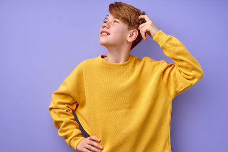 Portrait of pensive teen boy isolated on purple background. Thoughtful teenager holding hand on...