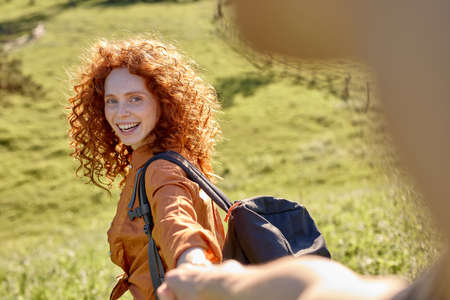 Follow me. Attractive curly woman takes mans hand, leads in the forest to hike, travel, smiling happily. Adorable beautiful caucasian lady enjoy travelling with boyfriend, lead active lifestyleの写真素材