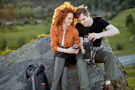 Happy couple having rest and relax on the head of mountain drinking tea, enjoying nature landscape...