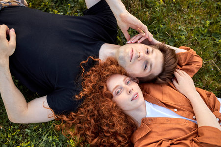 Top view on cute couple lying on grass in field at summer day, enjoying nature. Young man and woman...