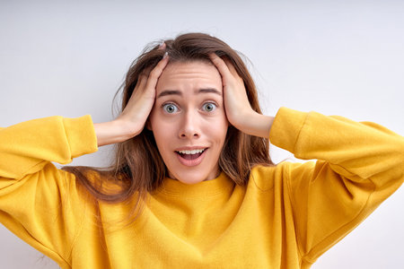 Emotional woman in panic grabs head and looks frustrated at camera realizes big failure poses...