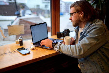 Caucasian young male photographer sitting with laptop and camera at cafe. Concept of modern...
