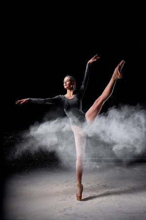 Dancer posing dancing gracefully in studio with cloud of dust, flour. flexible Dancer in black suit is moving, in action, having good choreographic training, raising leg up. ballet, performanceの写真素材