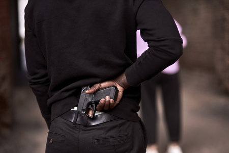 Robbery or criminal man in black hoodie is holding gun standing behind the woman, going to commit a...