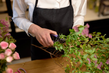 cropped female holding scissors while cutting flowers, preparing bouquet in flower shop....