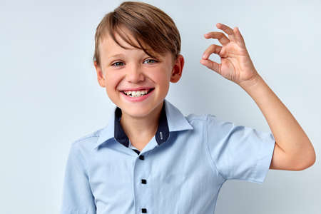 its OK. Positive child boy showing ok gesture, isolated on white studio background. Excited caucasian kid in shirt posing at camera, copy space for advertisement. young cheerful boy smilingの写真素材