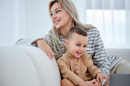 Carefree female parent have rest with preschooler son in living room wathcing cartoons, at home....