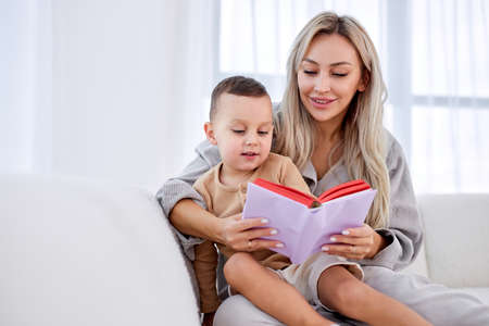 Happy caucasian cute little boy listening mother, reading funny story or fairy tales. relaxed beautiful woman having rest, spending leisure time, sitting on sofa with son, leisure time. in cozy roomの写真素材
