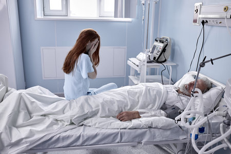 In Hospital, Worrying Young Mistress Sits Beside the Bed where Sick Man Lies. Redhead Woman Is...