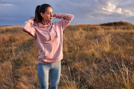 Enthusiastic lady is wearing hoodie hood looking at side at sunset or sunrise in contemplation,...