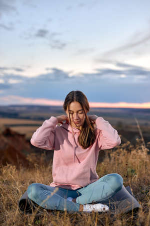 young woman is engaged in yoga, sitting on fitness mat outdoors. caucasian lady in sportive outfit enjoying healthy lifestyle, healthcare and wellbeing concept. peaceful woman keep calmの写真素材