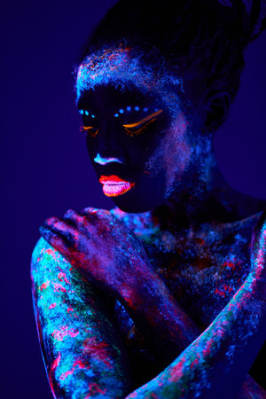 Sexual black female model posing with UV pattern on body, fluorescent body art make-up. peaceful calm beautiful lady is touching herself, enjoy the art and beauty. fantasctic interesting shoot.の写真素材